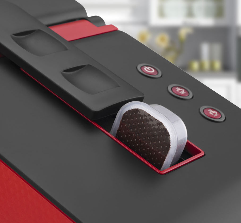 Closeup van een koffiecapsule die in een rode Chikko koffiemachine gaat